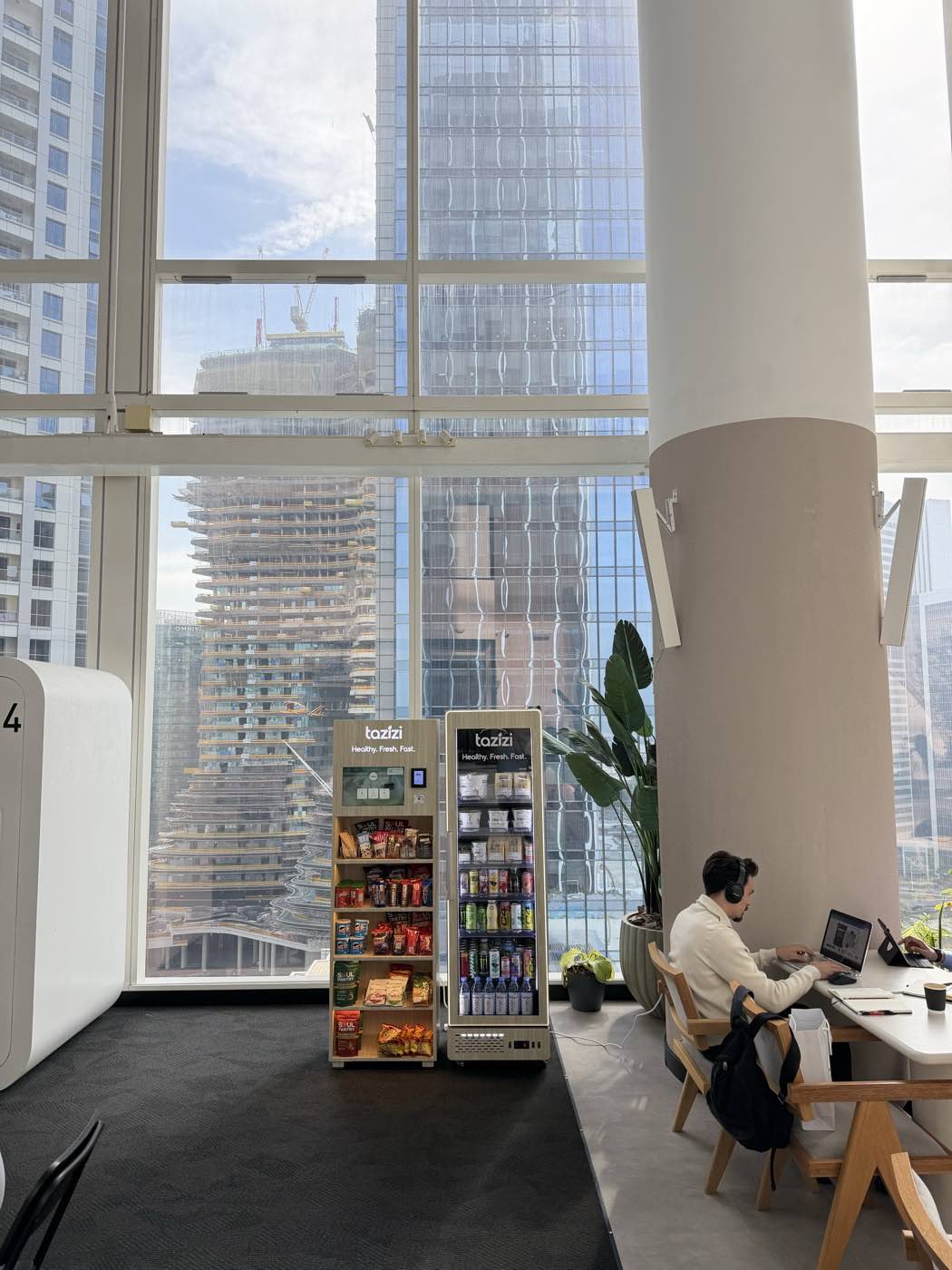 A Tazizi smart fridge in a Dubai office, with the Marina skyline through the window behind it